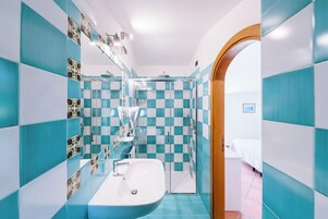 Un baño con baldosas azules y blancas formando un diseño de cuadros, un lavabo blanco y una zona de ducha.