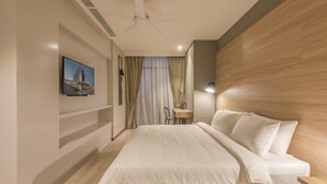 A hotel room with a large bed, a desk, a chair, a ceiling fan, and a painting on the wall.