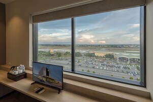 Habitación de hotel con un amplio ventanal que ofrece vistas al aeropuerto y edificios circundantes.