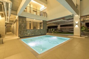 Una amplia piscina interior con un diseño de baldosas hexagonales, rodeada por un suelo de baldosas y una pared de piedra.