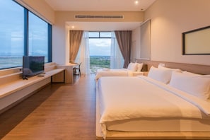 A hotel room with two beds, a TV on a bench, a desk, and a large window with a view.