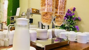 A buffet setup with a pitcher, plates, and cups, and a decorative vase with purple flowers. - Sem9 Senai (Senai)