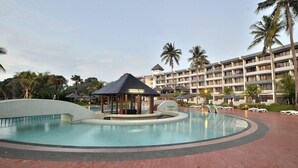 Un hotel con una grande piscina, palme e un edificio a più piani con balconi.