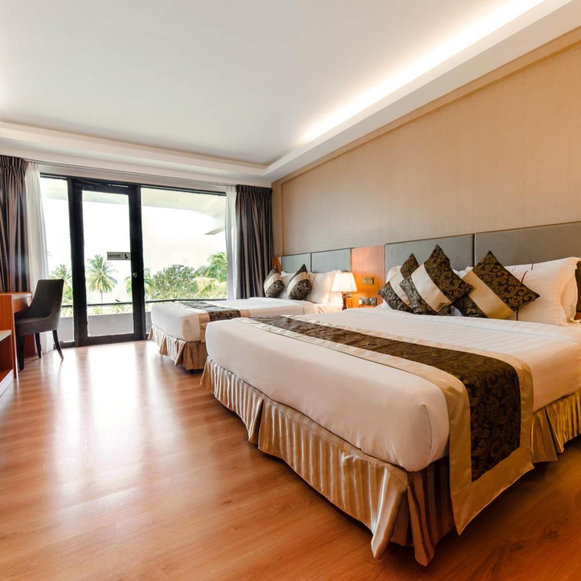 Habitación de hotel con una cama grande, un escritorio y vistas a palmeras a través de la ventana.