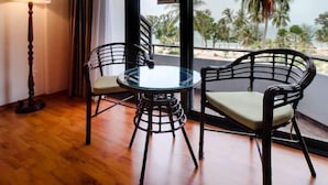 Un balcone con tavolo e sedie, una lampada e vista su palme e spiaggia.
