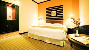 A hotel room with a bed, a desk, a chair, a nightstand, and a wall-mounted shelf with a vase of flowers. - Felda Residence Hot Springs (Ipoh)