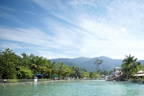Una piscina con uno scivolo acquatico, circondata da palme e con una montagna sullo sfondo.