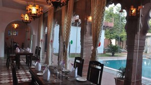 A restaurant with a checkered floor, wooden tables, and chairs, with a pool visible outside. - Amritara Chandra Mahal Haveli Bharatpur (Nadbai)