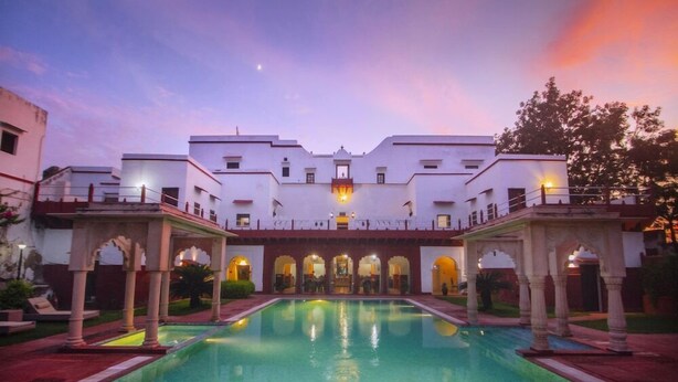 A large, rectangular swimming pool with a central water feature, surrounded by a covered walkway with arches. - Amritara Chandra Mahal Haveli Bharatpur (Nadbai)