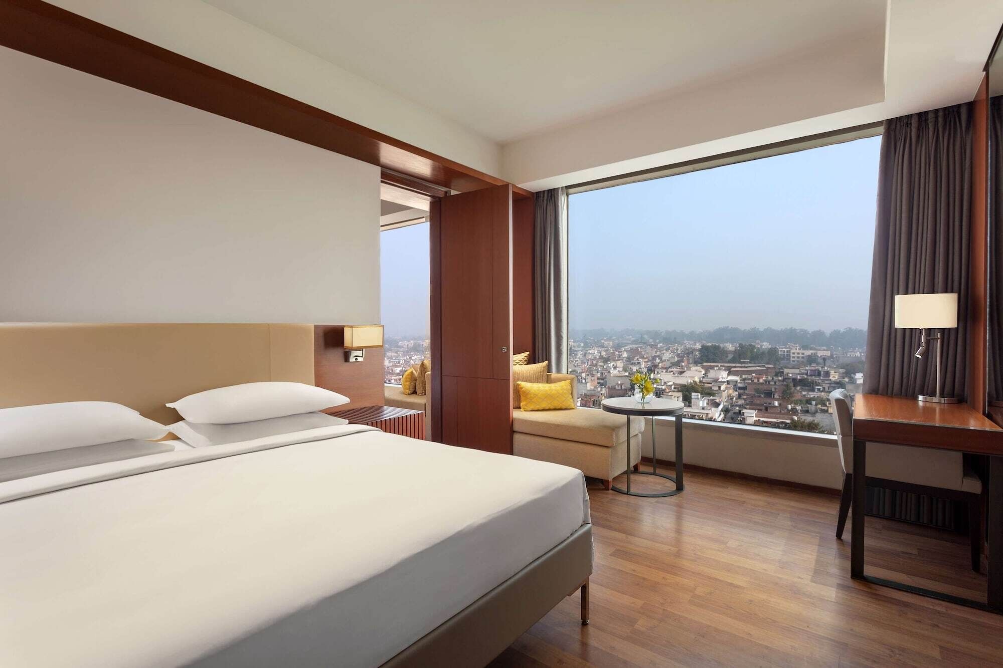 Habitación de hotel con una cama grande, un escritorio, una silla y vistas a un paisaje urbano.