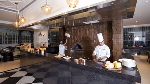 A modern kitchen with chefs preparing food, a brick oven, and a checkered floor. - Hyatt Regency Amritsar Hotel & Spa (Amritsar)