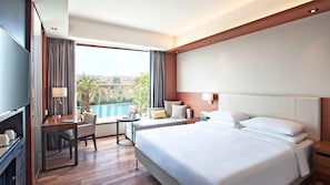 A hotel room with a large bed, a desk with a chair, a TV, and a view of a swimming pool. - Hyatt Regency Amritsar Hotel & Spa (Amritsar)