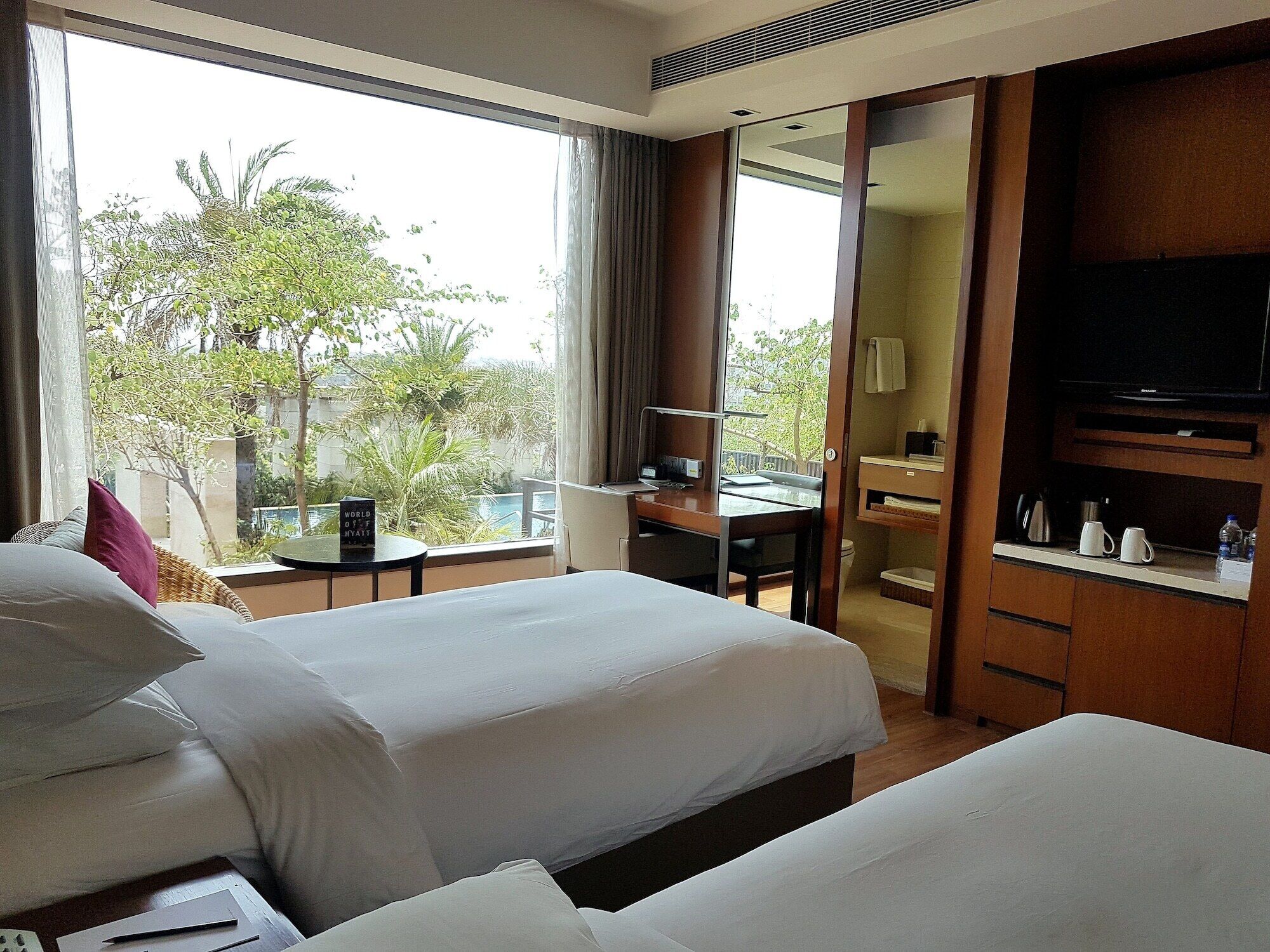 Ein Hotelzimmer mit zwei Betten, einem Schreibtisch, einem Fernseher und Blick auf Grünfläche.