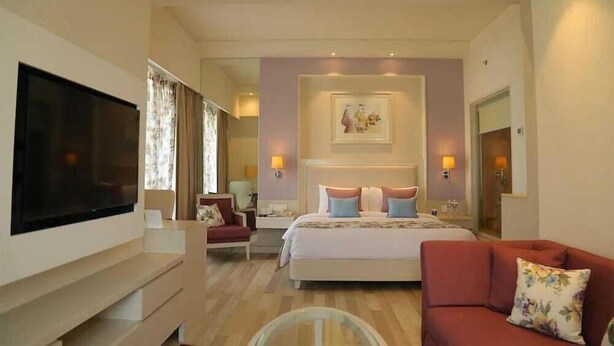 Une chambre d’hôtel avec un lit, une télévision, un canapé rouge et une table basse en verre.