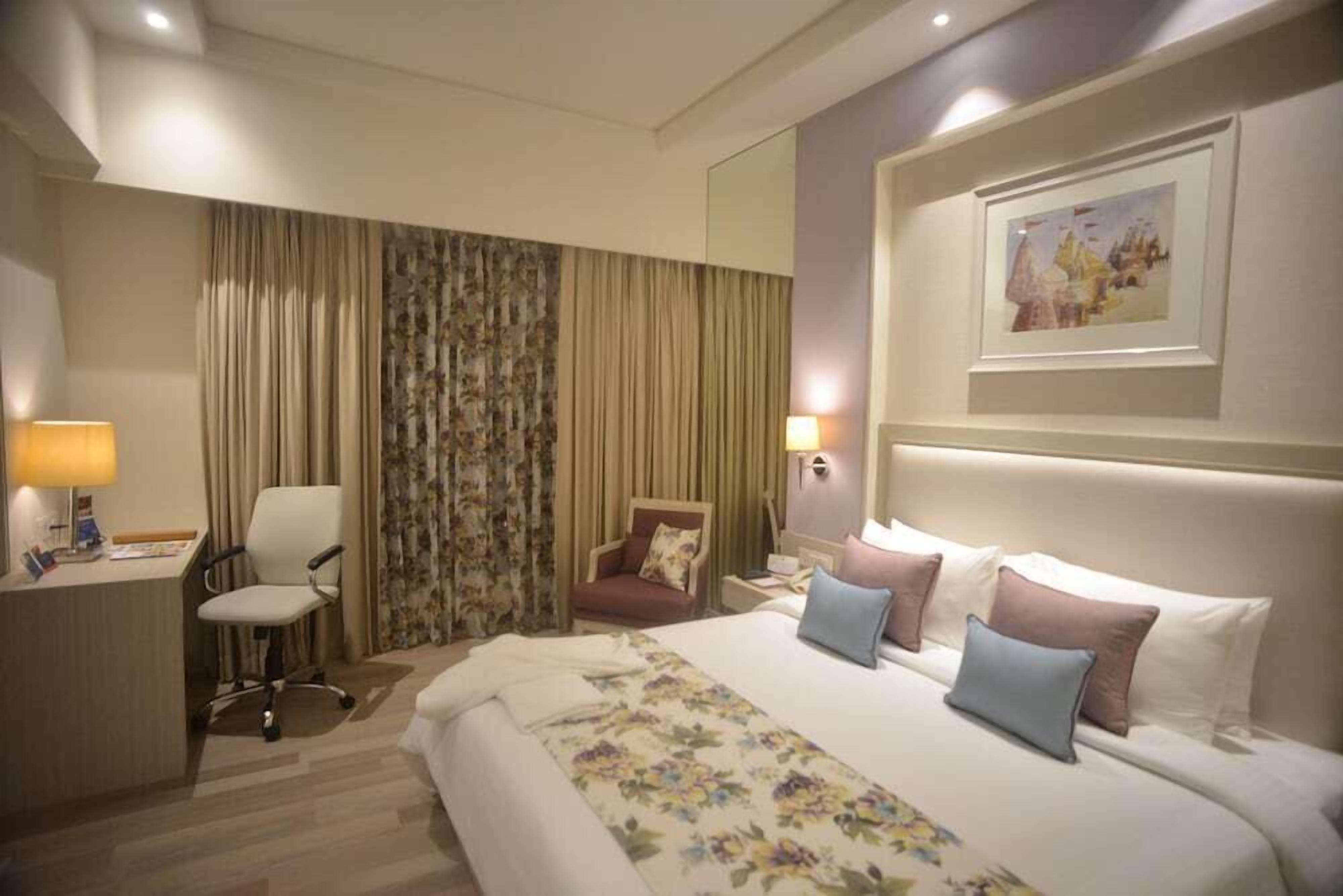 Une chambre d’hôtel avec un lit, un bureau, une chaise, une table de chevet et un tableau au mur.
