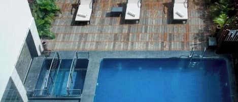 A rooftop pool area with lounge chairs and potted plants.