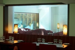 Ein Restaurant mit Sitzgelegenheiten in Form von Boxen und Tischen, einem großen Fenster und dekorativen Wandleuchten.