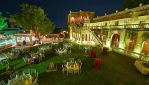 Un espace extérieur aménagé pour les repas, avec des tables et des chaises, un escalier et un bâtiment doté d’arcades et de balcons.