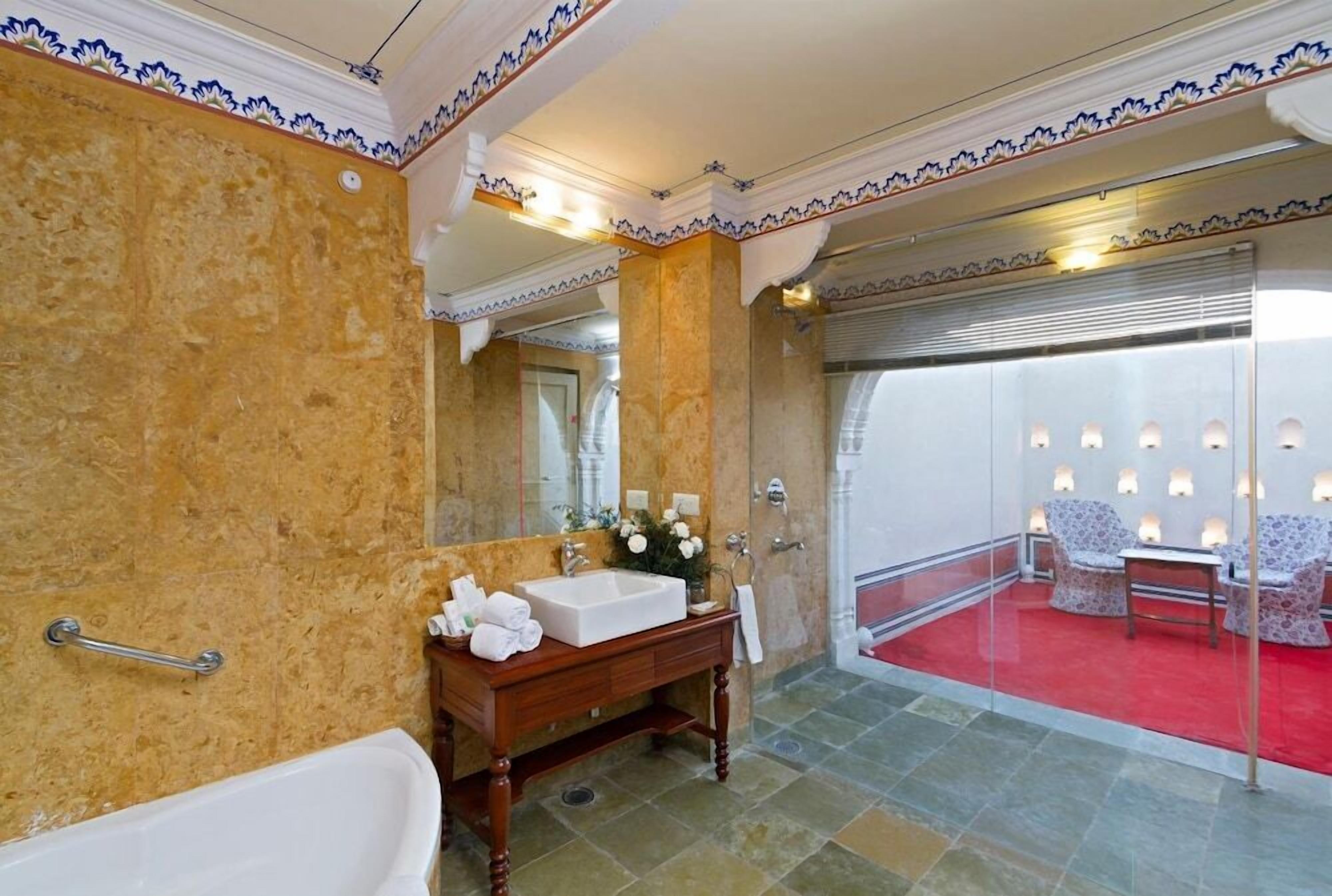 Ein Badezimmer mit Marmorwand, einem hölzernen Waschtisch, einer weißen Badewanne und einem roten Teppichbereich mit Sitzgelegenheiten.