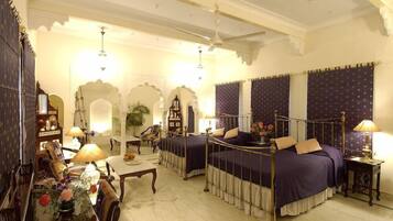 Una habitación tradicional con cama con dosel, una zona de estar con mesa y sillas, y una pared decorativa con arcos.