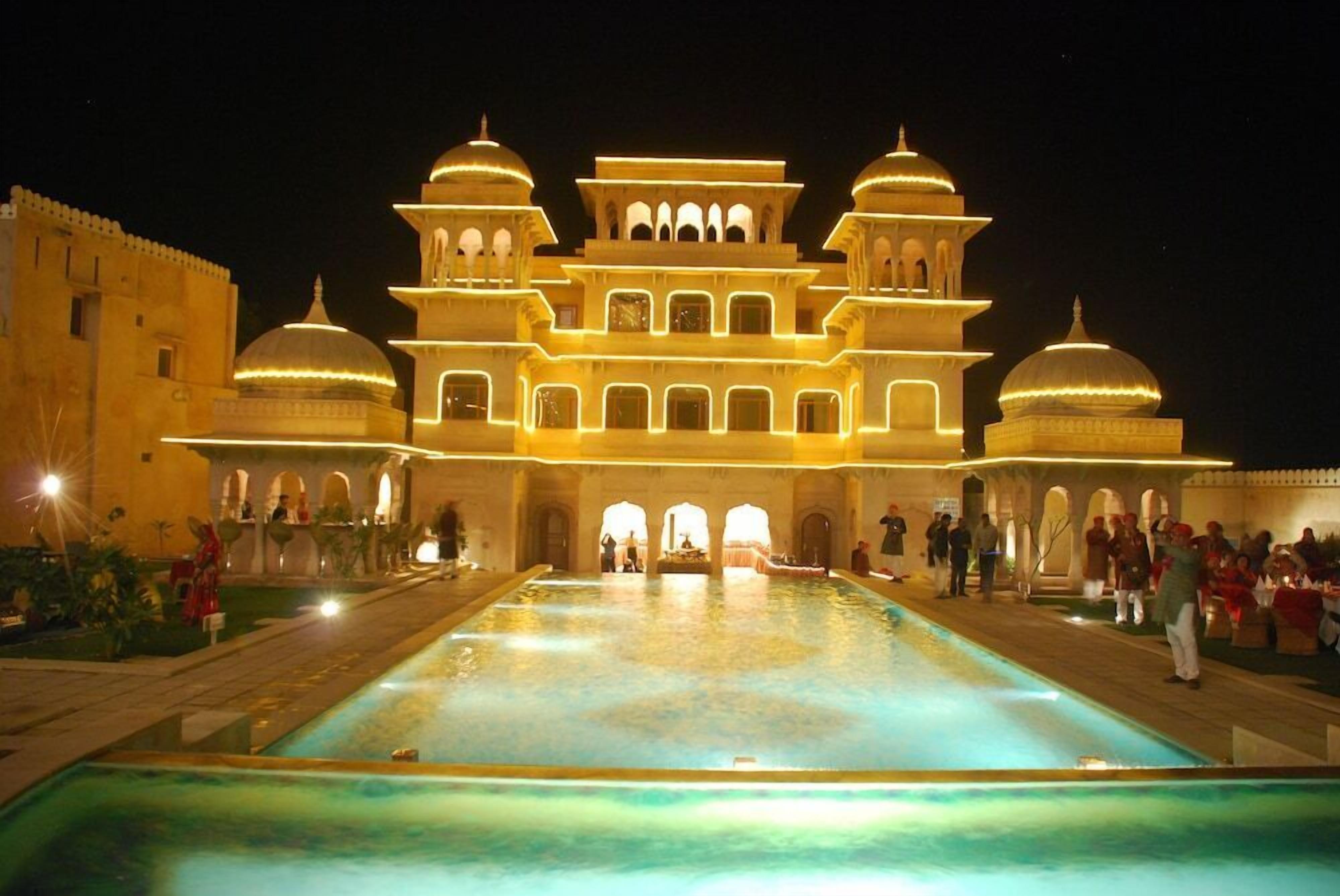 A grand building with multiple domes and arches, a large central pool, and people gathered around.