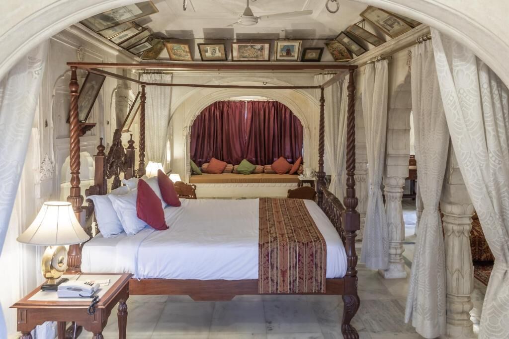 A four-poster bed with a canopy, a nightstand with a lamp, and a view of the room's architecture.