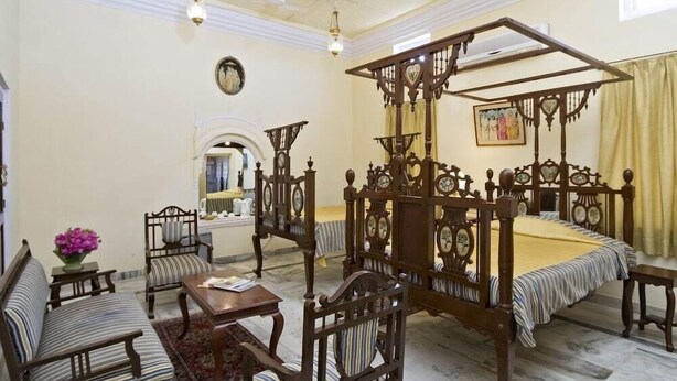 A traditional four-poster bed with a canopy, a sitting area with striped sofas, and a small table with a vase of flowers.