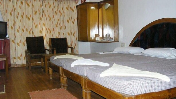 A room with a wooden bed, a chair, a mirror, and a patterned curtain. - Shanbhag Towers International (Hospet)