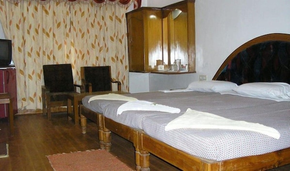 A room with a wooden bed, a chair, a mirror, and a patterned curtain. - Shanbhag Towers International (Hospet)