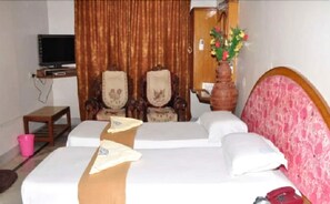A hotel room with a bed, two chairs, a small table, a television, and a vase with flowers. - Shanbhag Towers International (Hospet)