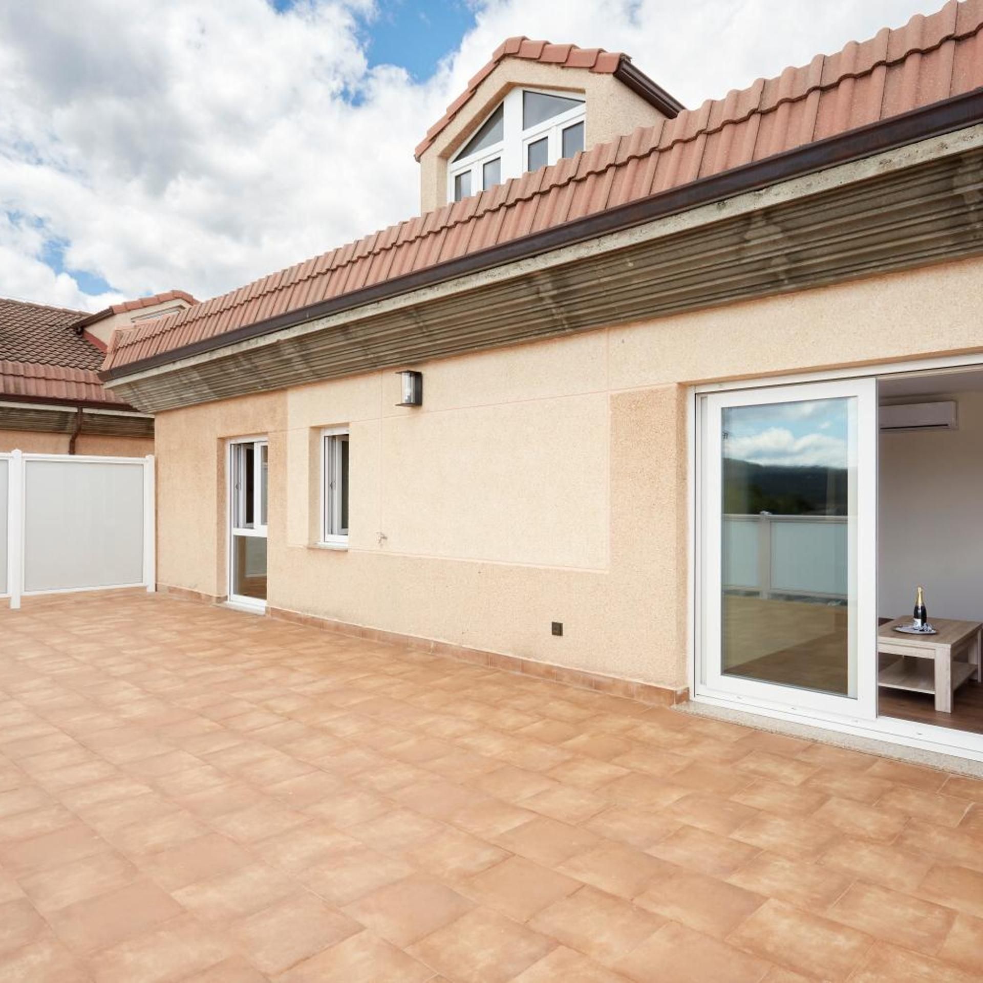 A residential building with a tiled roof, a covered patio area, and a sliding glass door leading to an interior space.