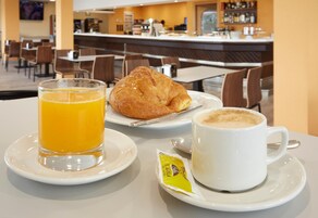 Mesa posta para o café da manhã, com um croissant, suco de laranja e uma xícara de café.
