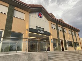Um hotel com fachada moderna, um letreiro grande com a palavra 'HOTEL' e placas indicando 'CAFÉ' e 'RESTAURANTE', sinalizando opções de refeições no local.