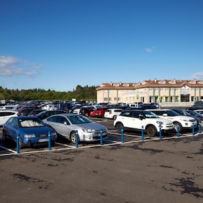 A parking lot with multiple cars and a hotel building in the background. - Cristal Aeropuerto (Castrillon)