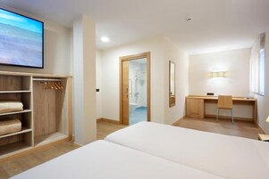 Quarto de hotel com cama, escrivaninha, cadeira, guarda-roupa e televisão.