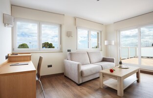 Uma sala de estar moderna com sofá, mesa de centro, escrivaninha e grandes janelas que oferecem vista do céu e árvores.