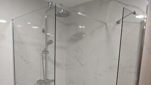 A glass-enclosed shower with a white marble wall and floor. - Cristal Aeropuerto (Castrillon)
