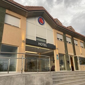 Un hotel con un llamativo letrero que dice 'HOTEL', una entrada de vidrio y un letrero de 'CAFETERÍA' que indica una zona de comedor.