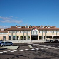 A hotel with a central entrance, multiple floors, and a parking lot with cars.