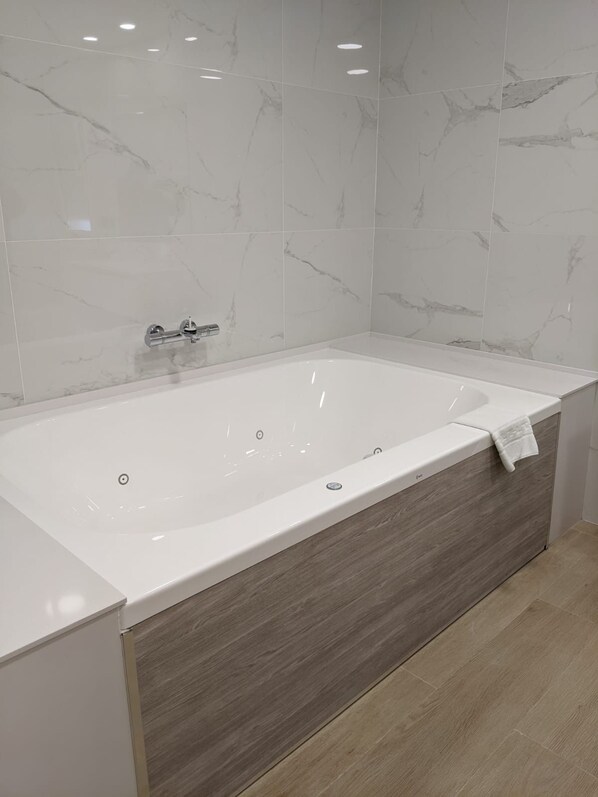A modern bathroom with a freestanding bathtub, marble tiles, and a wooden vanity. - Cristal Aeropuerto (Castrillon)