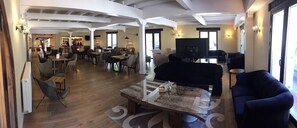 A spacious living area with a large sofa, a coffee table, and a dining area with multiple chairs and tables. There is a fireplace and a television in the background. - Cueva Del Fraile (Buenache de la Sierra)