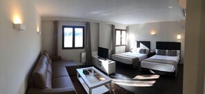 Ein Hotelzimmer mit einer Couch, einem Bett, einem Fernseher, einem Nachttisch und einem Fenster.