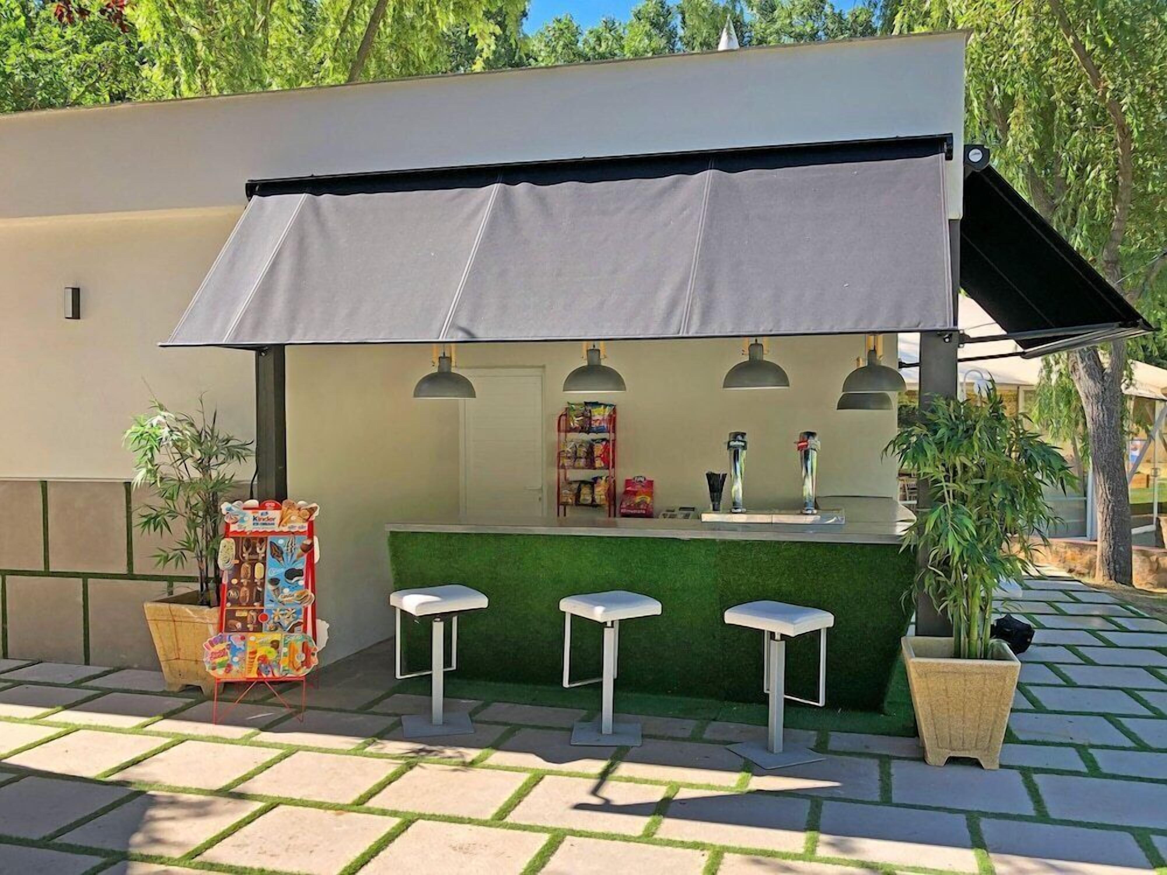 Un área de bar al aire libre con mostrador, tres taburetes y una marquesina.