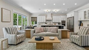 A modern kitchen with white cabinetry, a central island, and a dining area with striped chairs. - Spacious 7BR, New Build, Near Ocean, Private Pool, Elevator, Free Golf (Hilton Head Island)