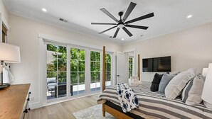 A bedroom with a bed, a ceiling fan, a TV, and a large window with a view of greenery. - Spacious 7BR, New Build, Near Ocean, Private Pool, Elevator, Free Golf (Hilton Head Island)