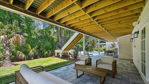 Eine Terrasse im Freien mit Holzmöbeln, einem Pool und Blick auf einen Garten.