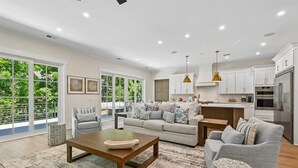 Eine moderne Küche mit weißen Schränken, Edelstahlgeräten und einem Essbereich mit grauem Sofa und Couchtisch.