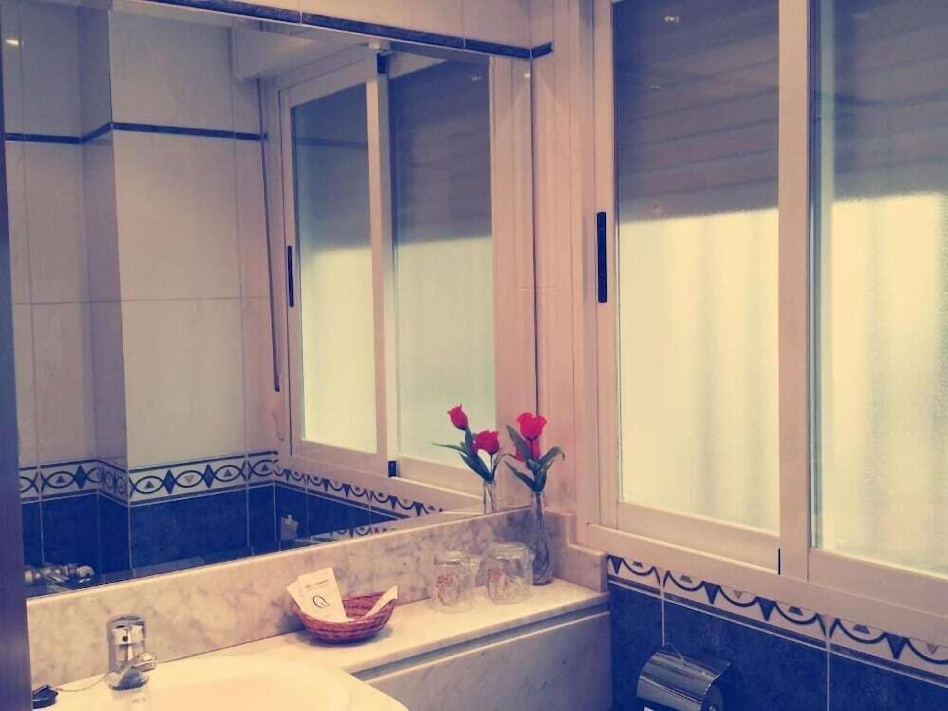 Une salle de bain avec un grand miroir, un lavabo et un vase rempli de fleurs.