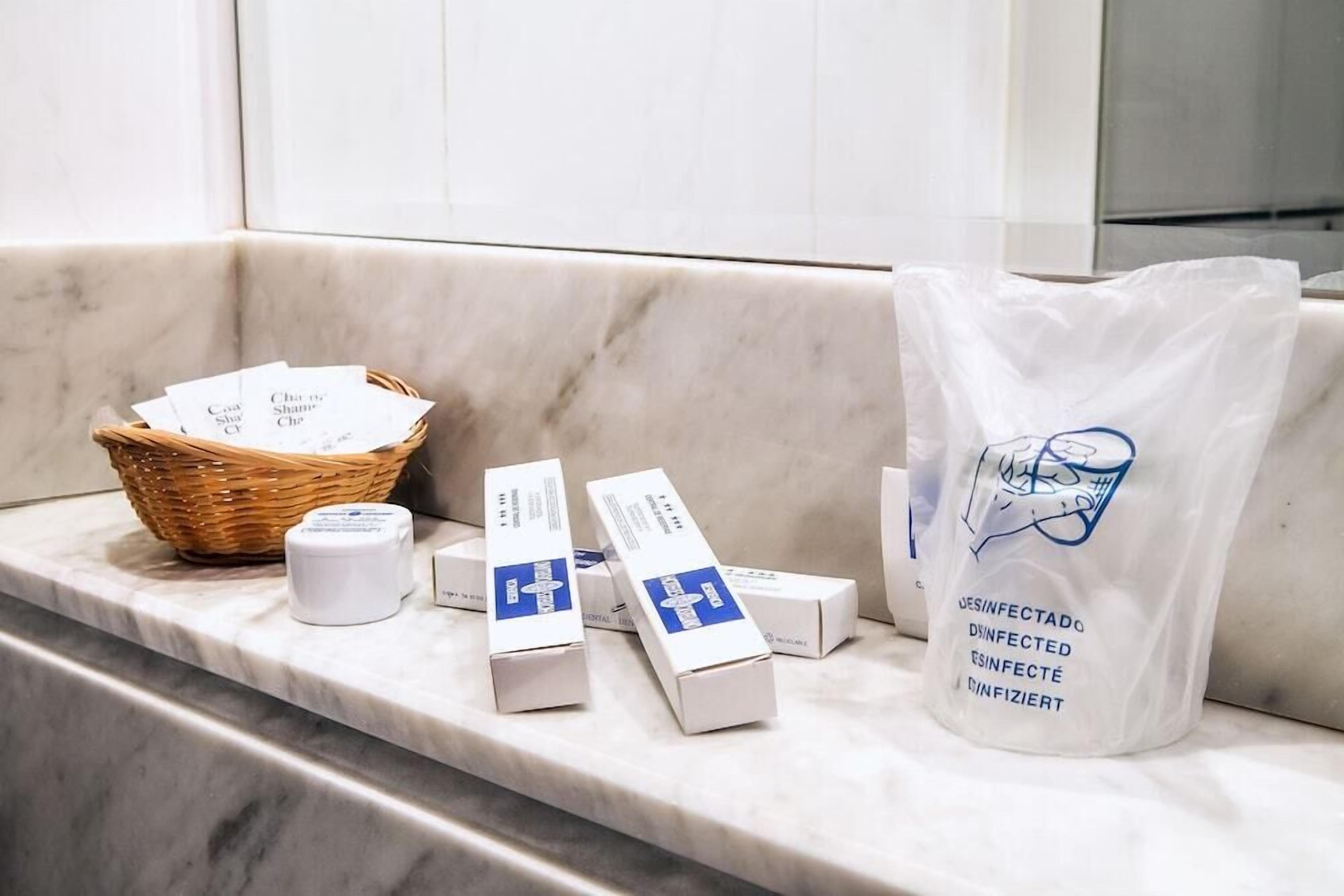 A marble counter with a basket of items, including boxes and a bag labeled "DESINFECTADO" and "DINFIZIERT".