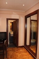 A room with a wooden floor, a television on a wooden table, and a bathroom visible through an open door.